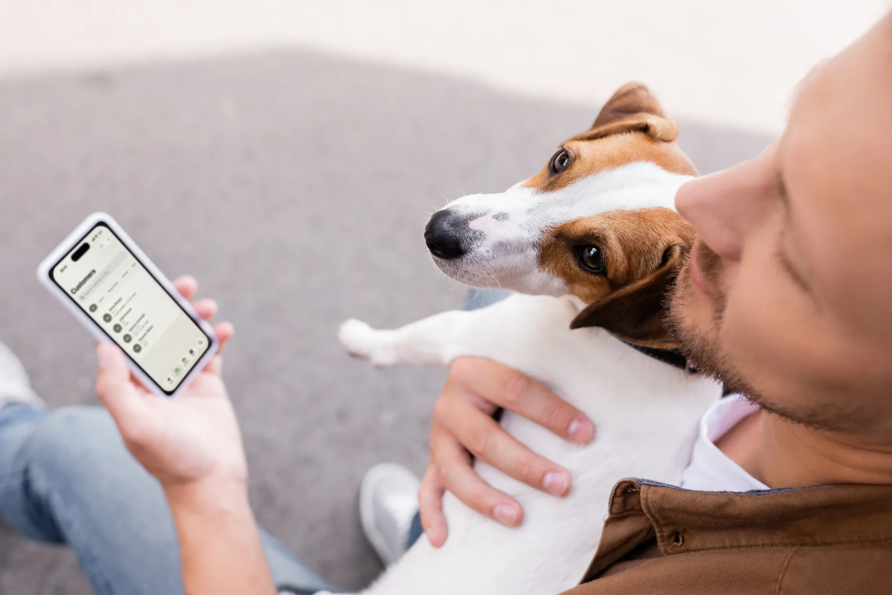 A man holds his Jack Russell in his arm, with the Dog Walkers client list open on his iPhone.
